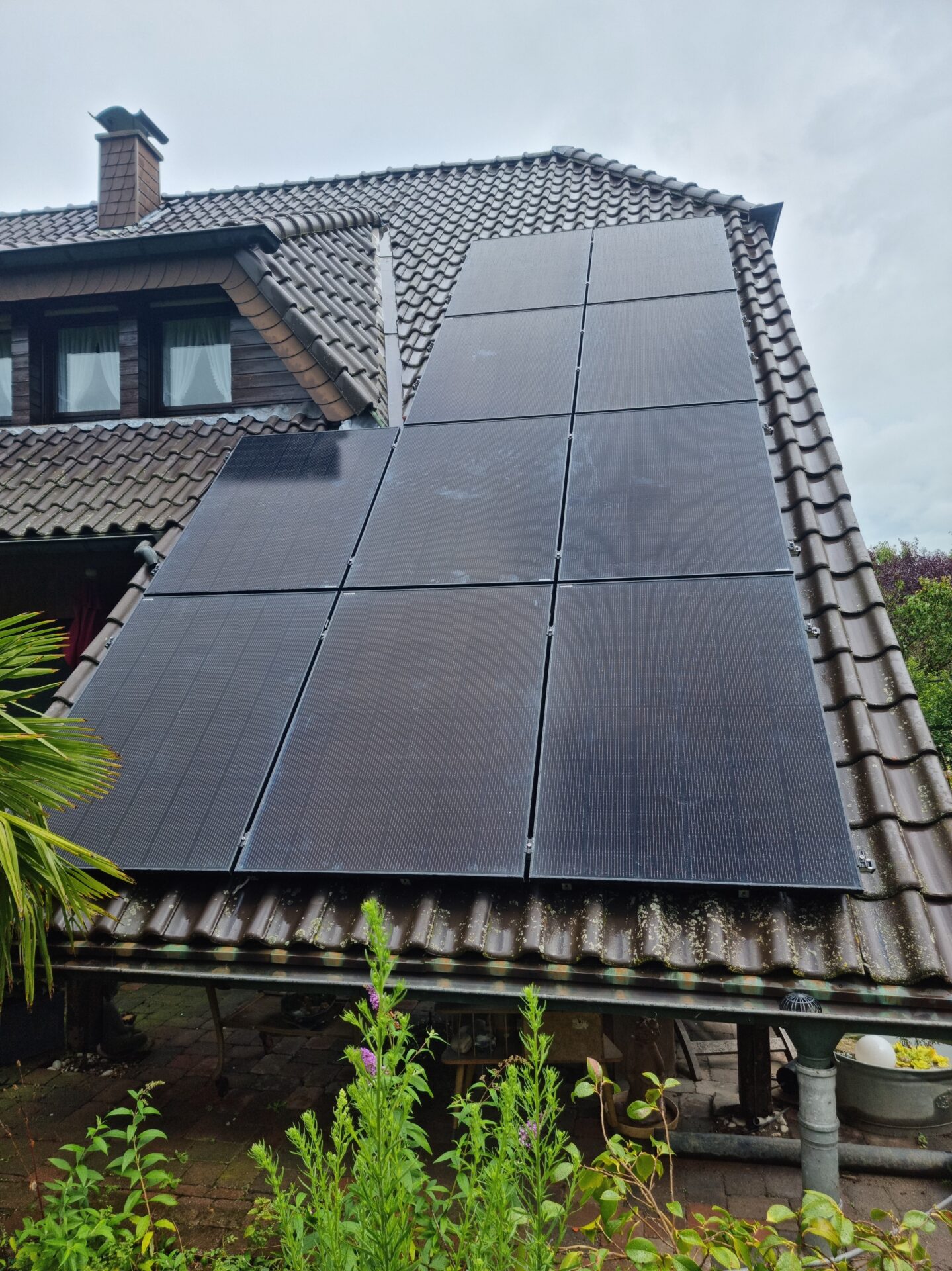 Hochformataufnahme einer großen Solar­anlage auf einem steilen Hausdach mit Garten im Vordergrund.