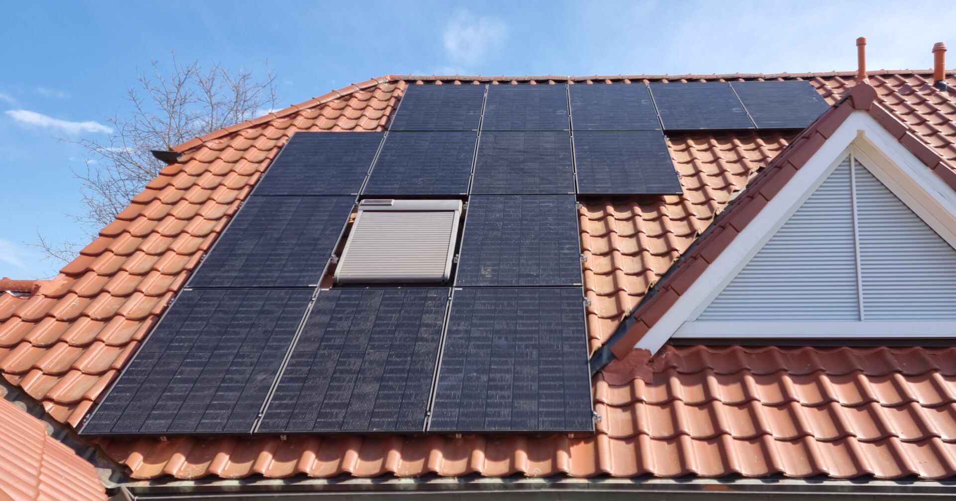Solar­module auf einem roten Sattel­dach mit blauem Himmel im Hintergrund.