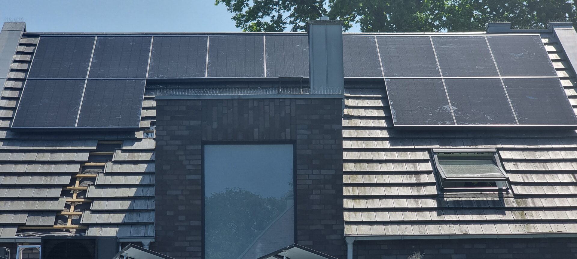 Dunkle Solarpanels auf einem grauen Ziegeldach über einem Eingangsbereich.